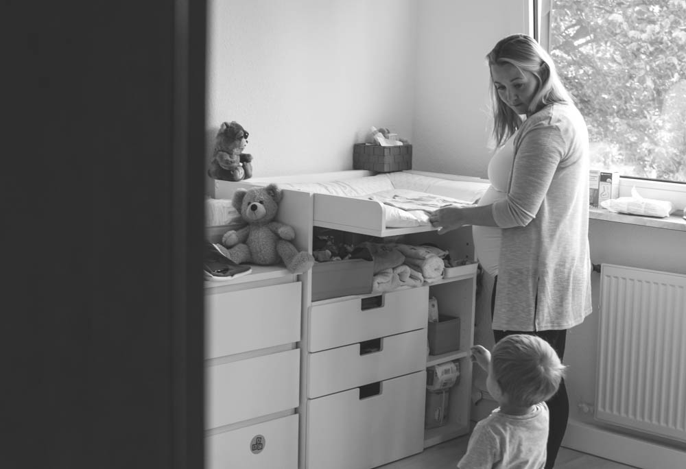 Mama mit babybauch schaut vom Wickeltisch zu ihrem 2 Jähringen Sohn