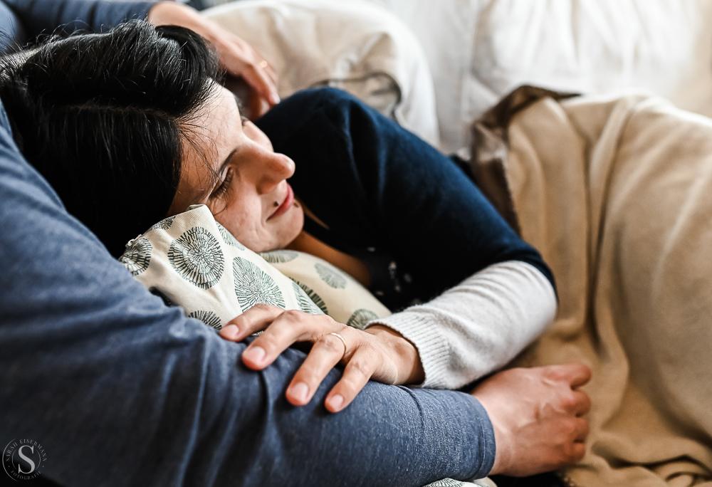 Frau schmiegt sich in Decke eingemuckelt auf dem Sofa in dem Arm ihres Mannes